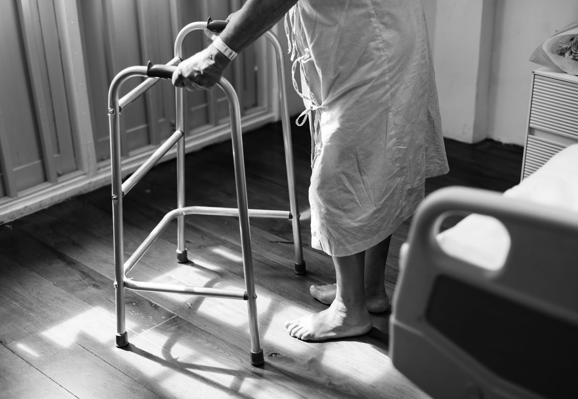 person holding medical walker beside white hospital bed